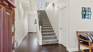 Un escalier menant à un deuxième étage, une porte en bois avec une poignée en laiton et un cadre photo fixé au mur.