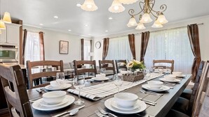 Une salle à manger avec une longue table dressée pour six personnes, des chaises en bois et un lustre.