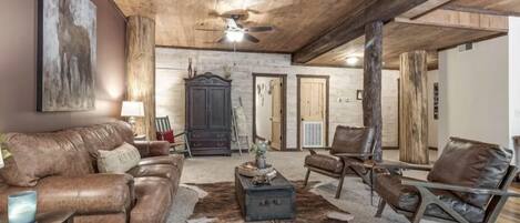 A spacious living room with leather furniture, a wooden ceiling, and a large rug.