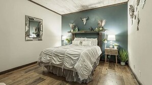 A bedroom with a bed, a mirror, a wall-mounted shelf with decorative items, and a wooden floor. - The Log Palace Private Guest Suite 2 Bedroom Cabin by RedAwning (Cottontown)