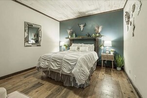 Un dormitorio con cama, un espejo, un estante en la pared con objetos decorativos y suelo de madera.