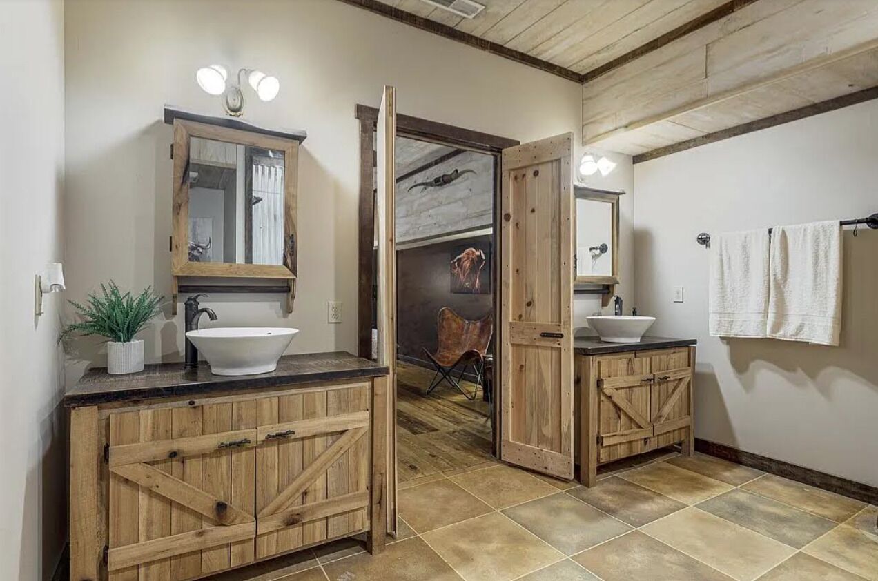 Ein rustikales Badezimmer mit Holzschränken, einem großen Spiegel und einem weißen Waschbecken.