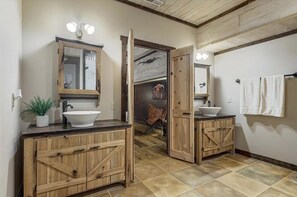 Een landelijke badkamer met houten kastjes, een grote spiegel en een witte wastafel.