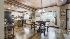 A spacious kitchen with wooden flooring, a dining area with a wooden table and chairs, and a stone accent wall. - The Log Palace Private Guest Suite 2 Bedroom Cabin by RedAwning (Cottontown)