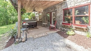 A covered patio area with a stone wall, outdoor seating, and a hot tub. - The Log Palace Private Guest Suite 2 Bedroom Cabin by RedAwning (Cottontown)