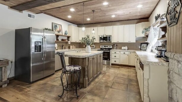 A kitchen with a central island, stainless steel appliances, and a rustic ceiling. - The Log Palace Private Guest Suite 2 Bedroom Cabin by RedAwning (Cottontown)