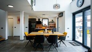 A modern dining area with a wooden table and black chairs, a kitchen in the background, and a large window with a view of the outside. - Modern Villa Noel with swimming pool (Valica)