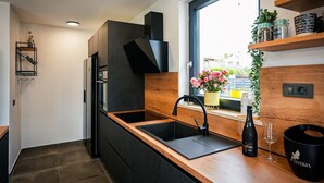 A modern kitchen with black cabinetry, a wooden countertop, a black sink, and a window with a view of buildings outside. - Modern Villa Noel with swimming pool (Valica)