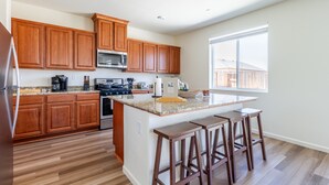 A modern kitchen with wooden cabinets, a granite countertop, and a large island with bar stools. - 5BR Home Hard Rock Casino & Beale AFB Area (Marysville)