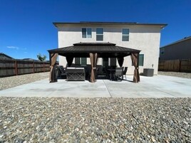 Un patio cubierto con mobiliario exterior, una pérgola y una casa al fondo.