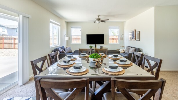A dining room with a large table set for six, surrounded by wooden chairs, a ceiling fan, and a TV mounted on the wall. - 5BR Home Hard Rock Casino & Beale AFB Area (Marysville)