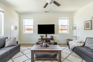 Una sala de estar con un televisor de pantalla plana, dos sofás, una mesa de centro y un ventilador de techo.