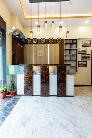 A reception area with a marble floor, a reception desk with a wooden panel design, multiple clocks, and hanging pendant lights. - Hotel Imperial (Mumbai)