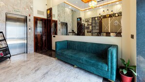 A lobby with a teal sofa, an elevator, a reception desk, and a large mirror reflecting the interior. - Hotel Imperial (Mumbai)