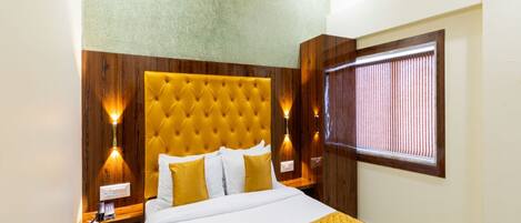 A hotel room with a large bed, wooden headboard, bedside lamps, and a window with blinds.