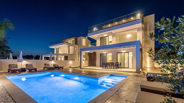 Ein modernes, zweistöckiges Haus mit Pool, Außenbereich zum Sitzen und einer gut beleuchteten Terrasse.