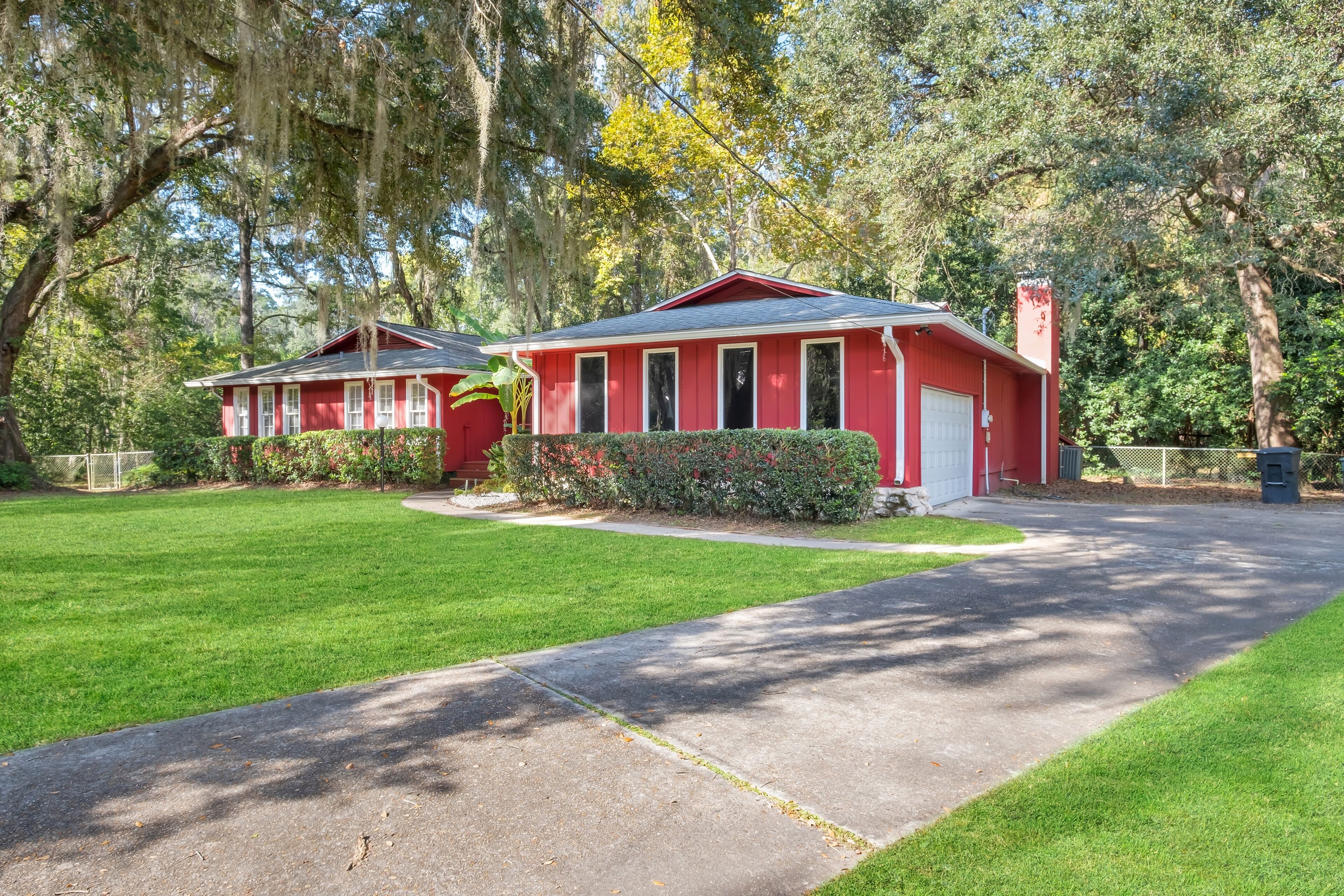 A red house with a white garage door, surrounded by a well-maintained lawn and trees.