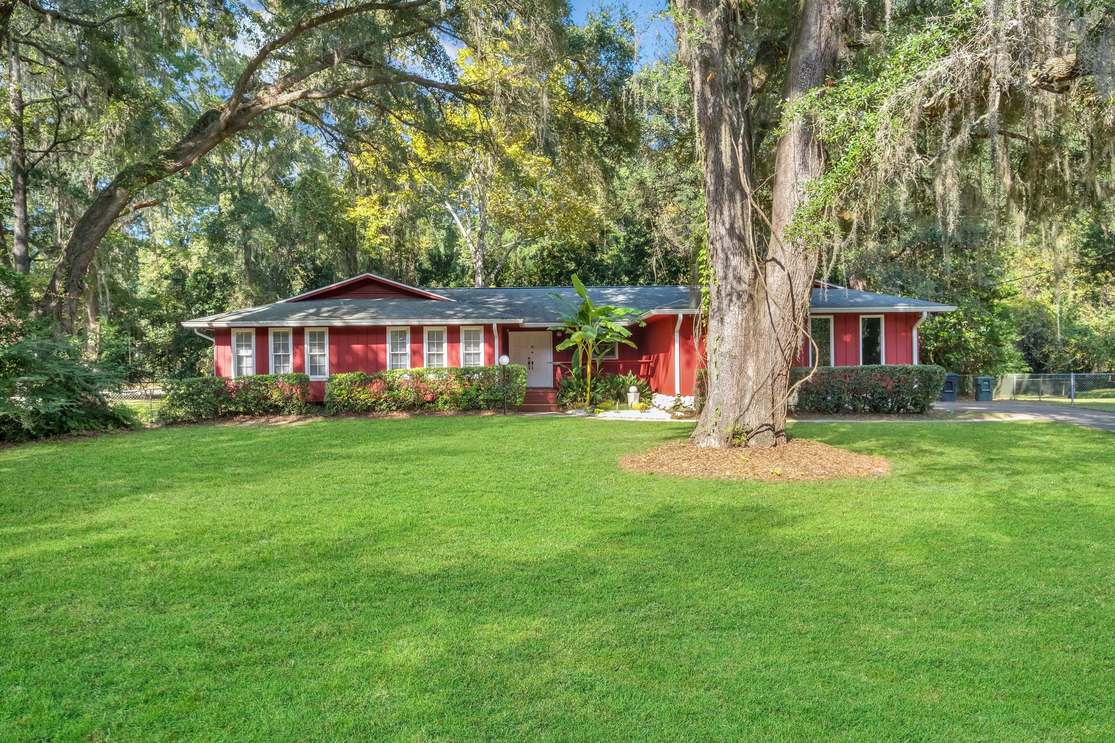 Une maison rouge avec une pelouse bien entretenue et de grands arbres.