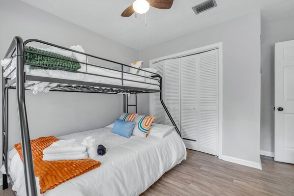A bunk bed with white bedding, a wooden ceiling fan, and a white door in the background.