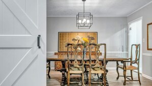 A dining area with a wooden table and chairs, a chandelier, and a large painting on the wall.