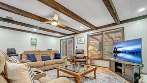 A living room with a beige sofa, a glass coffee table, a TV, and a wooden ceiling.