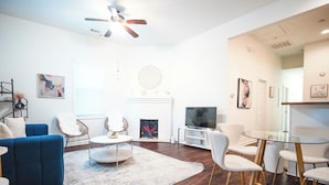 A modern living room with a blue sofa, white chairs, a glass coffee table, and a fireplace.