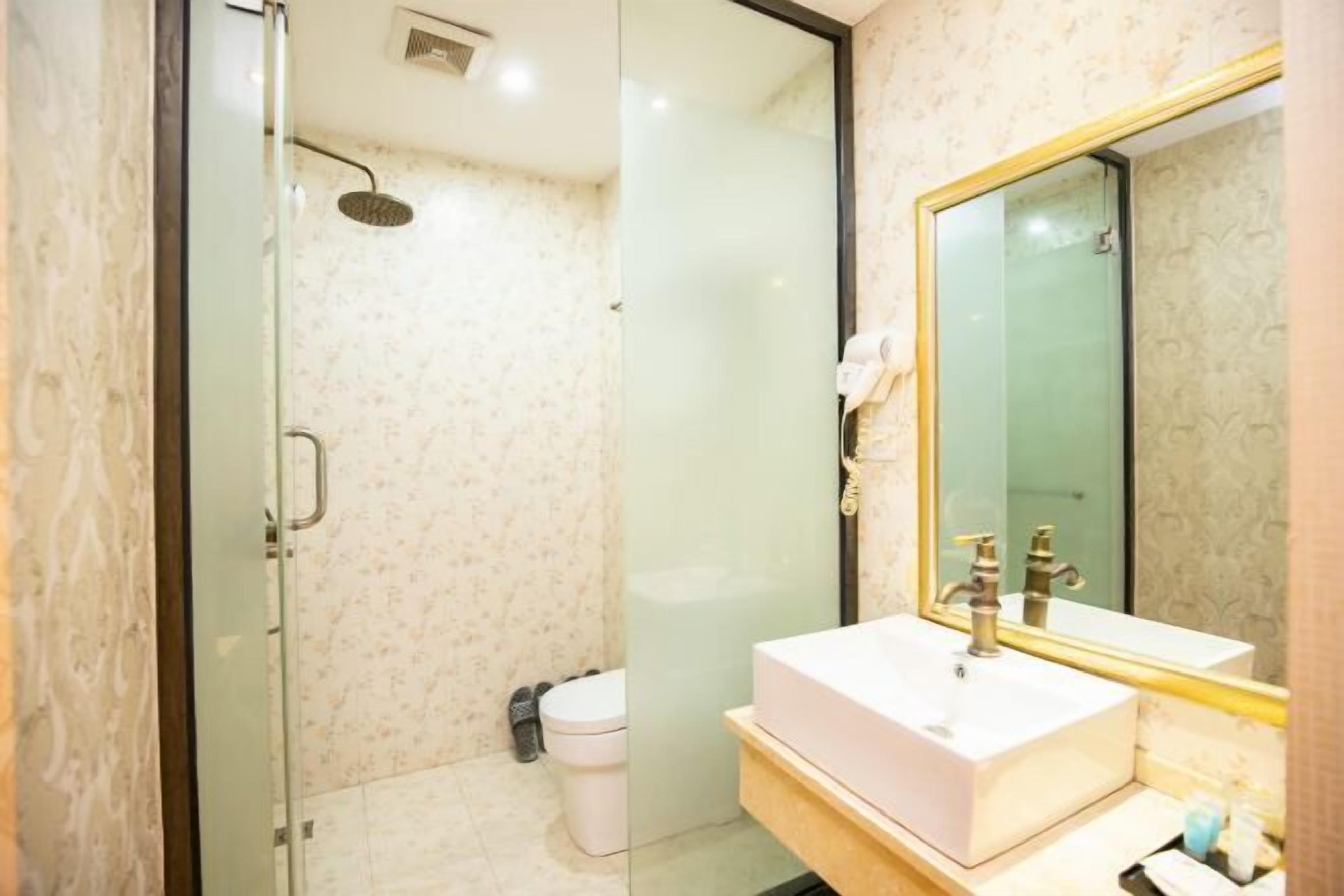 A modern bathroom with a glass-enclosed shower, a white sink, and a large mirror with a gold frame.
