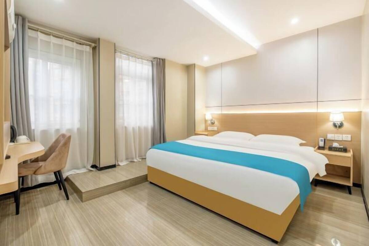 A hotel room with a bed, bedside tables, a desk, and curtains.
