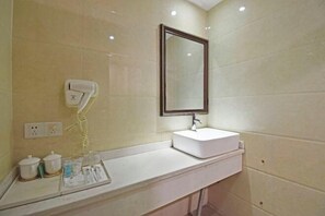 Un baño con lavamanos blanco, un espejo, secador de pelo y artículos de aseo en la encimera.