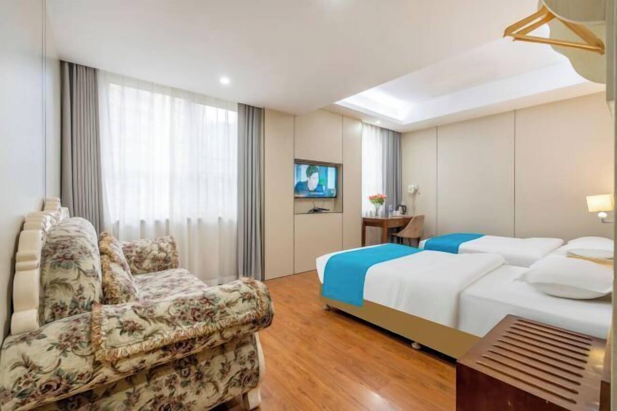 A hotel room with a sofa, a bed with blue bedding, a TV, and a desk.