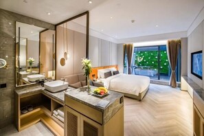 Una camera d'albergo moderna con un letto grande, un bagno con un angolo trucco, uno specchio ampio e vista sul verde all'esterno.