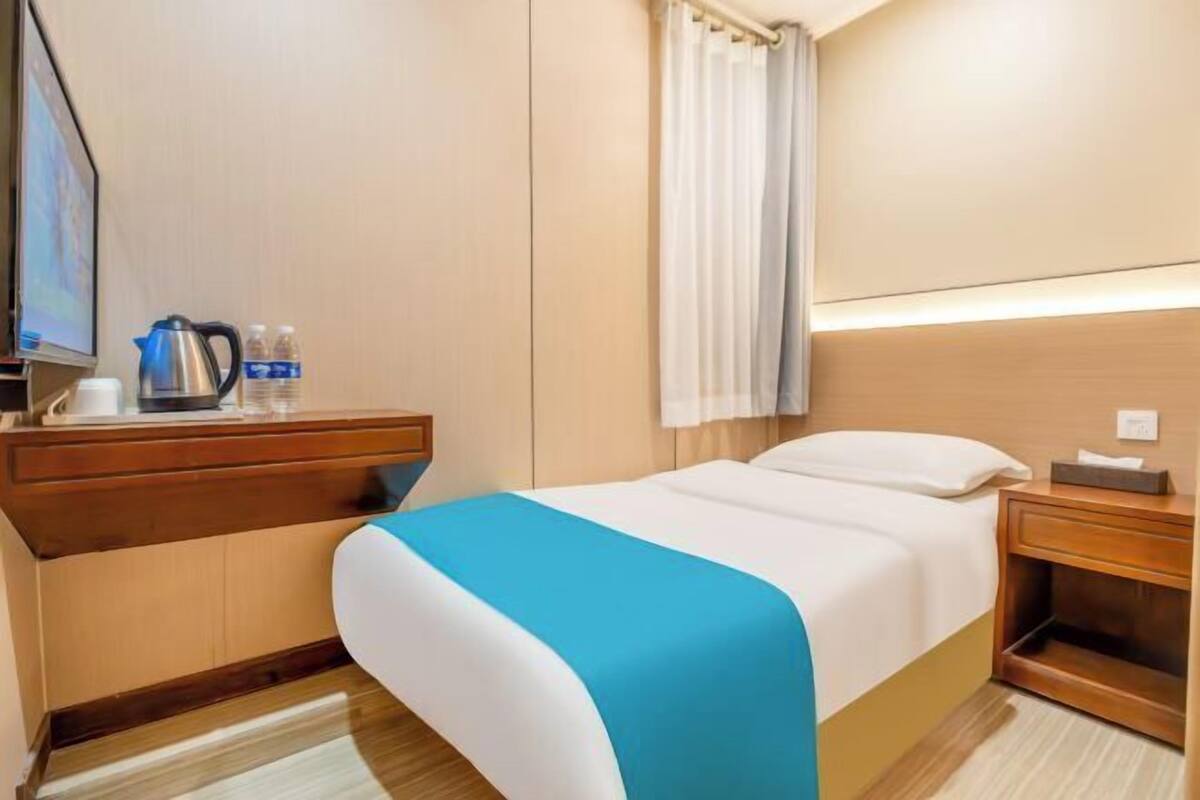 A hotel room with a bed, a bedside table with a lamp, a TV, and a window with curtains.