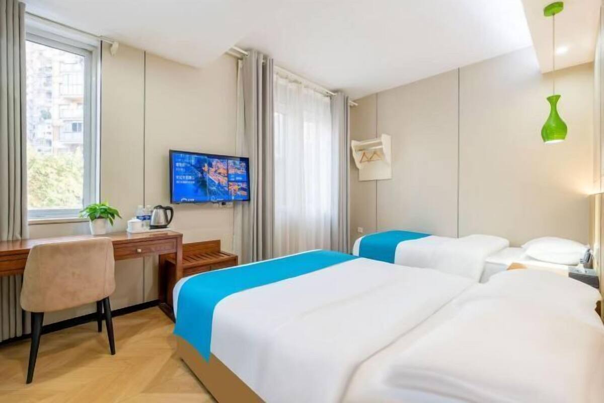 A hotel room with a desk, two beds, a TV, and a window with curtains.