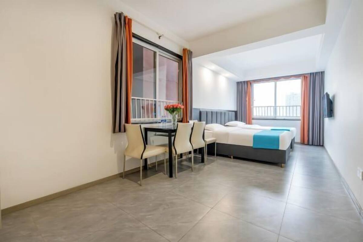A hotel room with a bed, a desk with chairs, a window, and a TV on the wall.