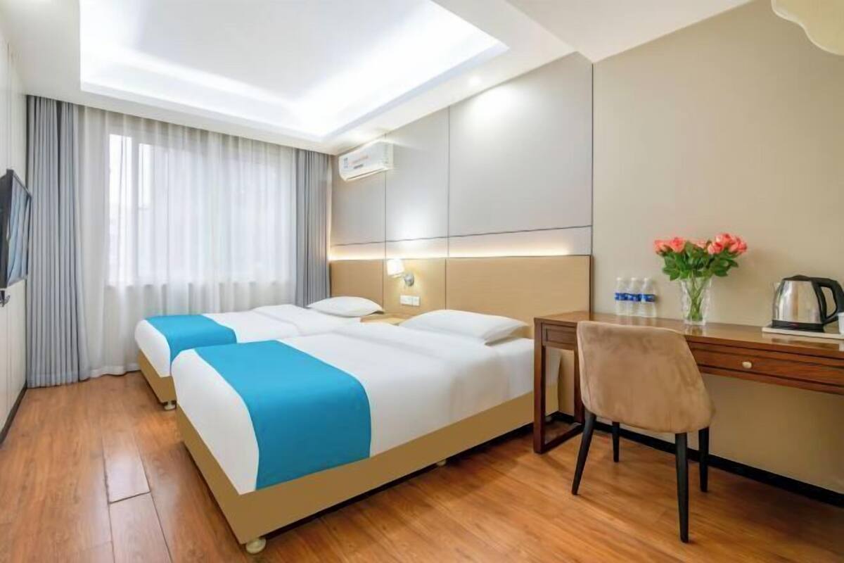 A hotel room with two beds, a desk, a chair, a TV, and a window with curtains.