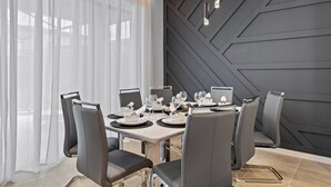 Et moderne spiseområde med et geometrisk vægdesign, et stort vindue med lette gardiner, og et spisebord med stole.