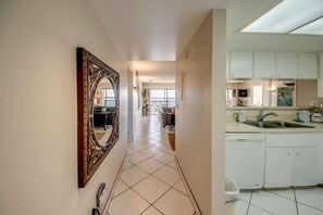 A hallway leading to a kitchen with white cabinets, a tiled floor, and a large mirror on the wall.