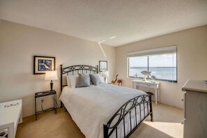 A bedroom with a bed, bedside tables, a desk, a chair, a window with a view, and a dresser.