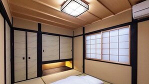 A traditional Japanese-style room with tatami flooring, a bed, sliding doors, and a window with a grid pattern. - Rinn Marikoji (Kyoto)