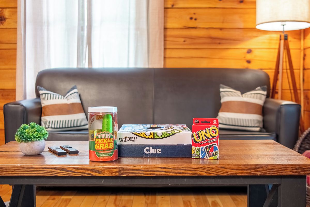 A wooden table with a jar of pickles, a box of Clue, and a UNO game box.