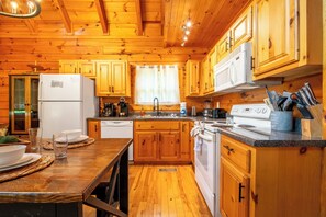 Une cuisine de style rustique, avec des éléments en bois, comprenant une table en bois, des placards, un réfrigérateur, une cuisinière et un évier.