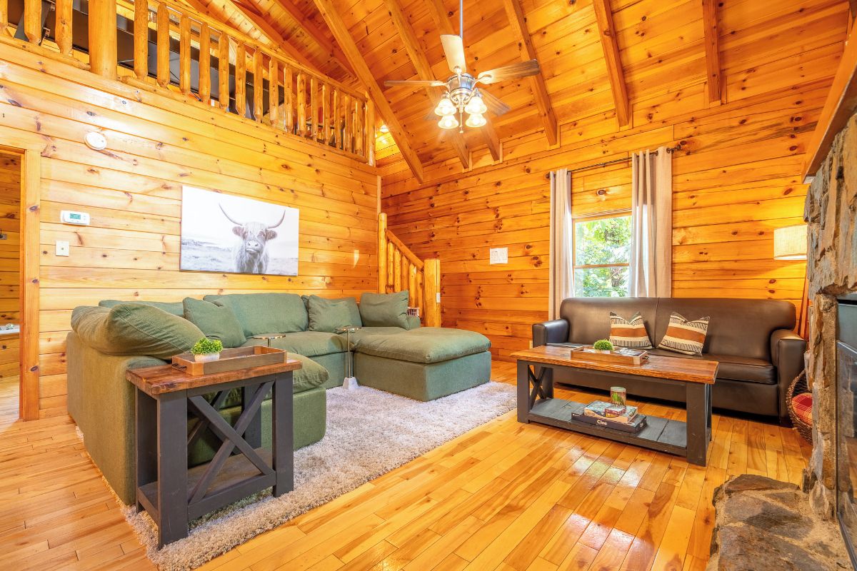A cozy cabin interior with a wooden ceiling, a fireplace, a green sofa, and a wooden coffee table.