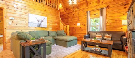 L’intérieur d’un chalet accueillant, avec un plafond en bois, une cheminée, un canapé vert et une table basse en bois.