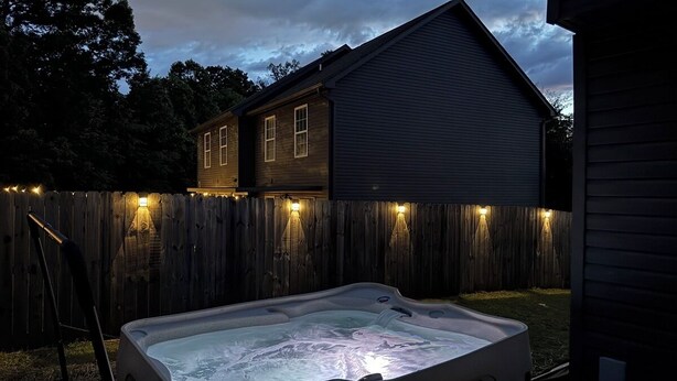 Un jacuzzi dans un jardin, avec une clôture en bois et une maison en arrière-plan.