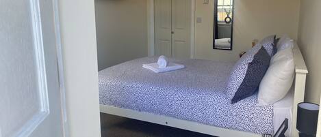 A bedroom with a bed, a TV mounted on the wall, a door, and a mirror.