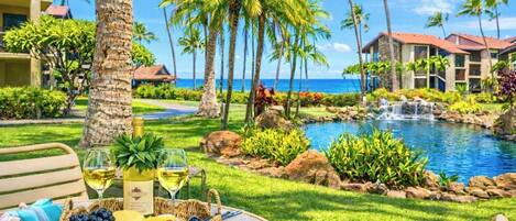 Un complexe hôtelier tropical avec une piscine, des palmiers et un espace repas où une table est dressée pour deux personnes.