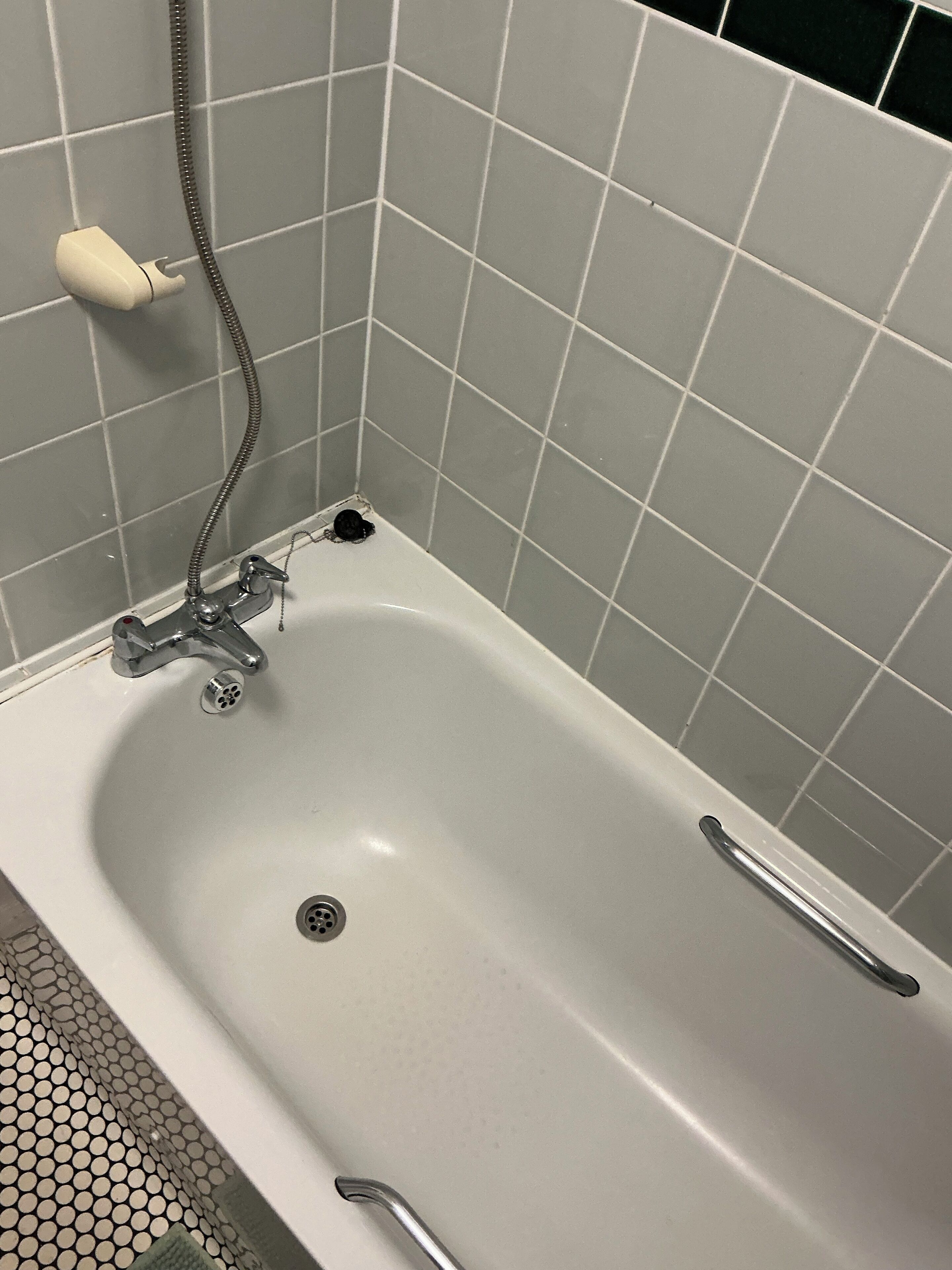 A bathroom with a white bathtub, a handheld showerhead, and a handheld faucet.