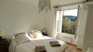 Quarto com cama, abajures, janela com cortinas e vista para o verde lá fora.