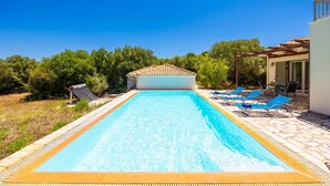 Una piscina con borde de baldosas, una zona techada con techo de cerámica y un patio con mobiliario exterior.