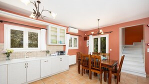 Una cocina con armarios blancos, una mesa de comedor con sillas, una araña y una escalera.
